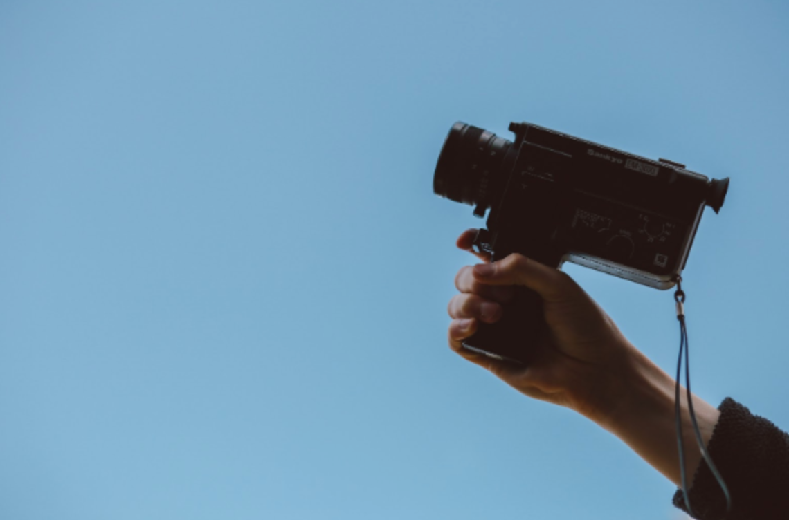 Hand holding a film camera against blue sky